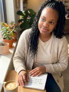 Leslieann at a sunny café table with The Mindful Journey Journal