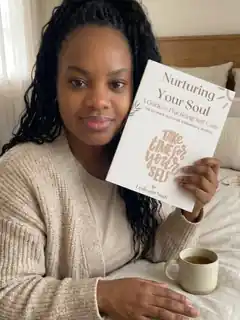 Leslieann on her bed holding up Nurturing Your Soul beside a cup of tea